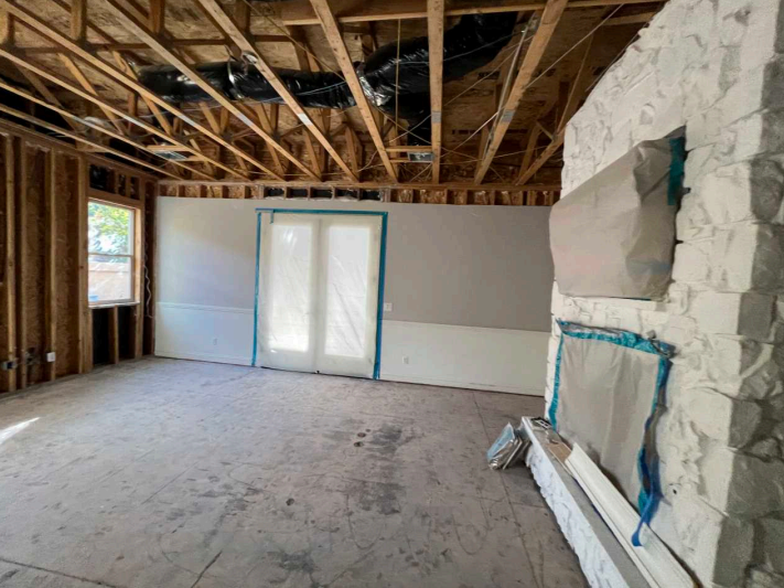 Partially renovated room with exposed ceiling beams, drywall, and a stone fireplace surround