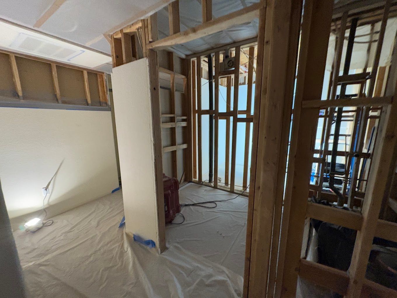 Interior under renovation with exposed wall framing, unfinished drywall, and plastic-covered floors