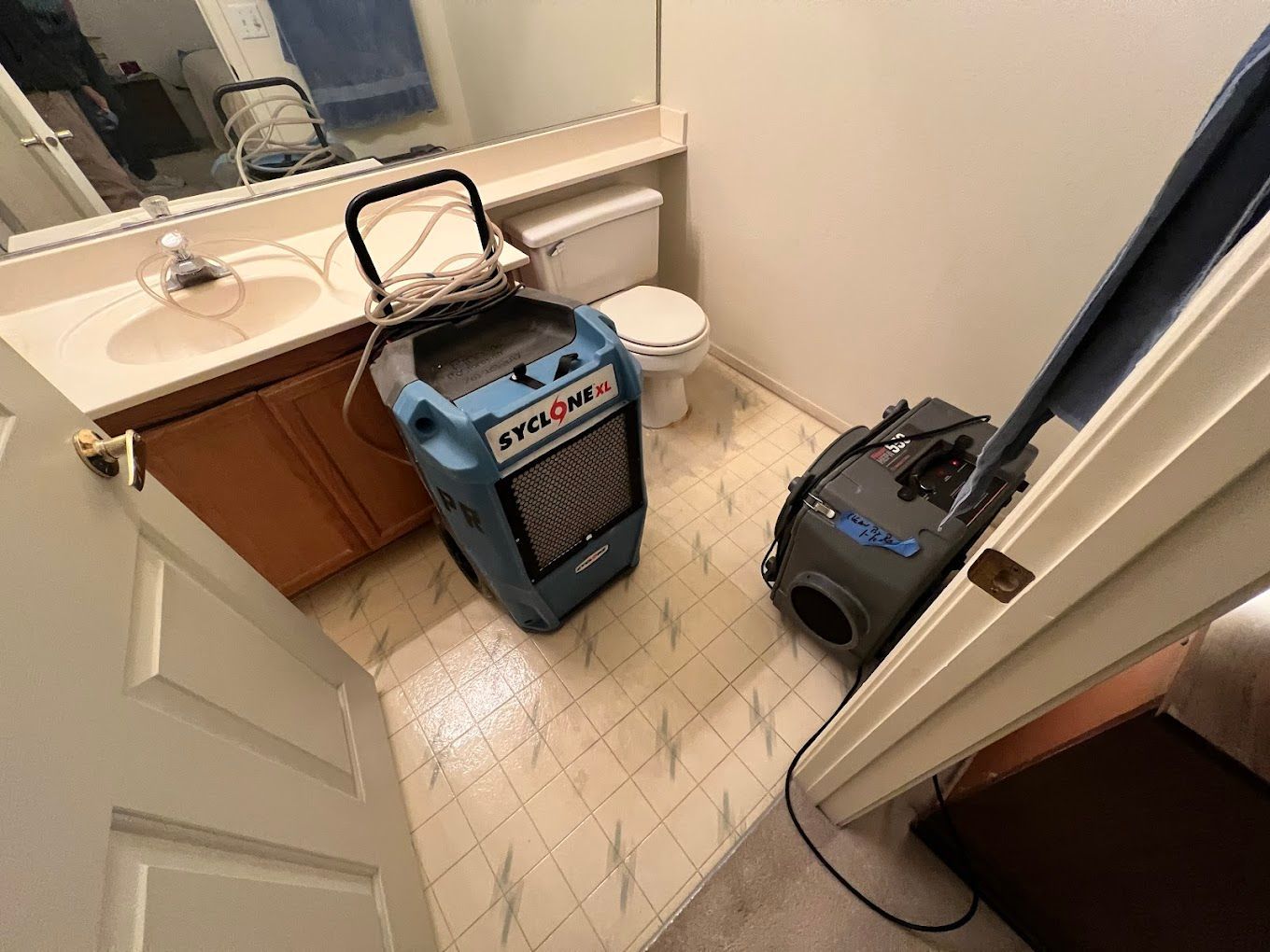 Bathroom with a blue dehumidifier and a black vacuum on tile floor near the sink