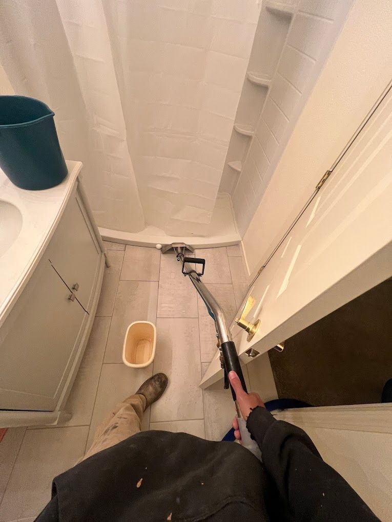 Person using a vacuum in a small bathroom beside a toilet and trash bin