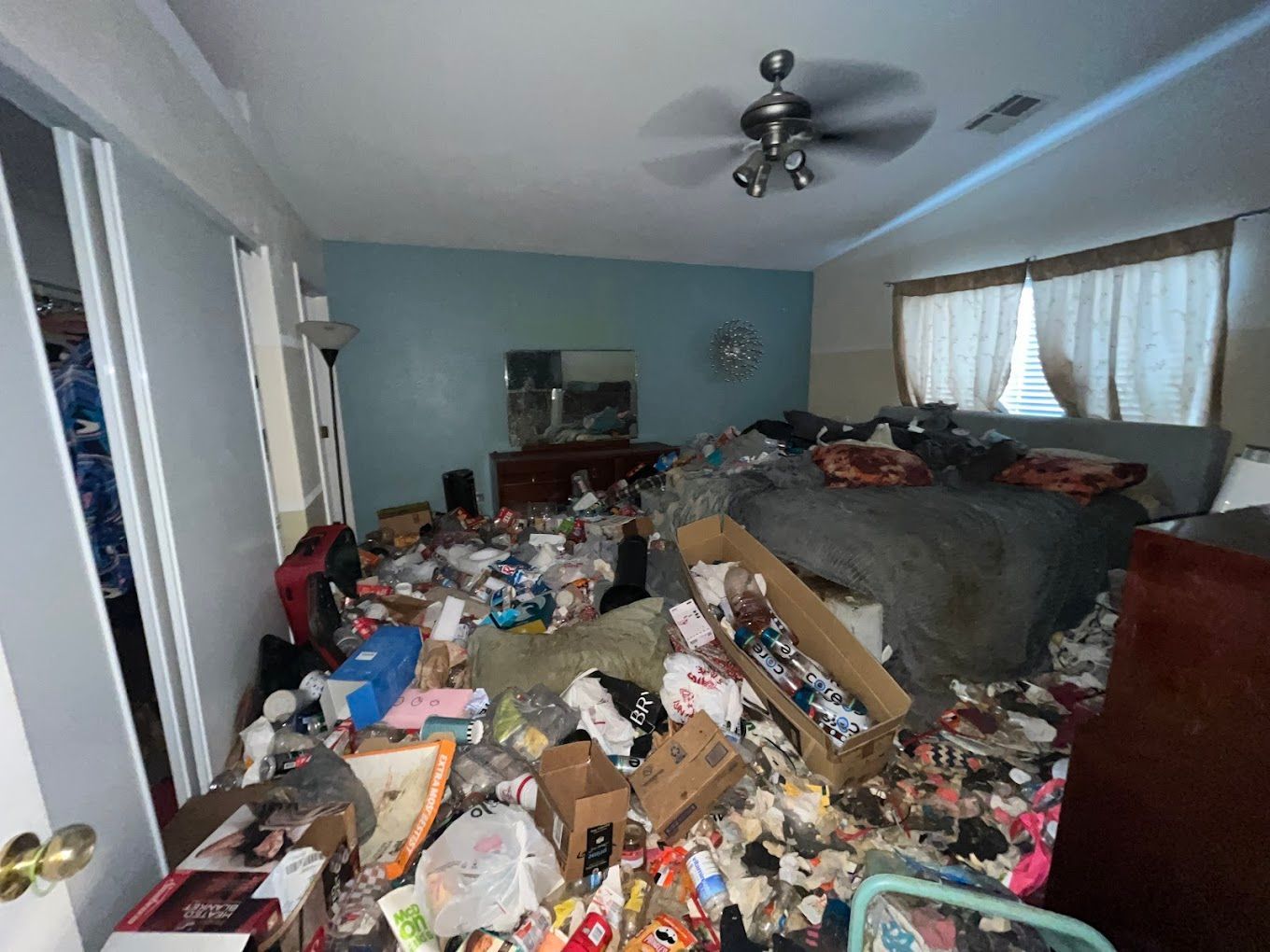 Cluttered bedroom with piles of trash and belongings covering the floor and bed