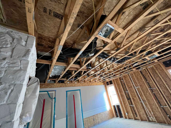Unfinished attic ceiling with exposed wood framing, insulation, and a partially covered wall.