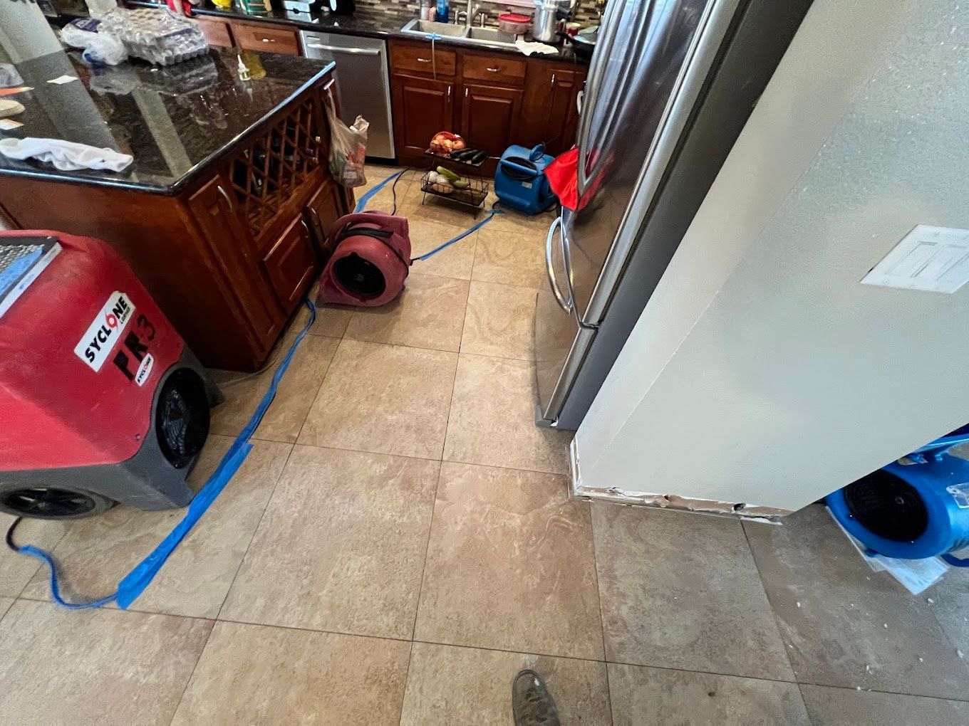 Cluttered kitchen floor with loose tiles, appliances, cords, and a small vacuum cleaner