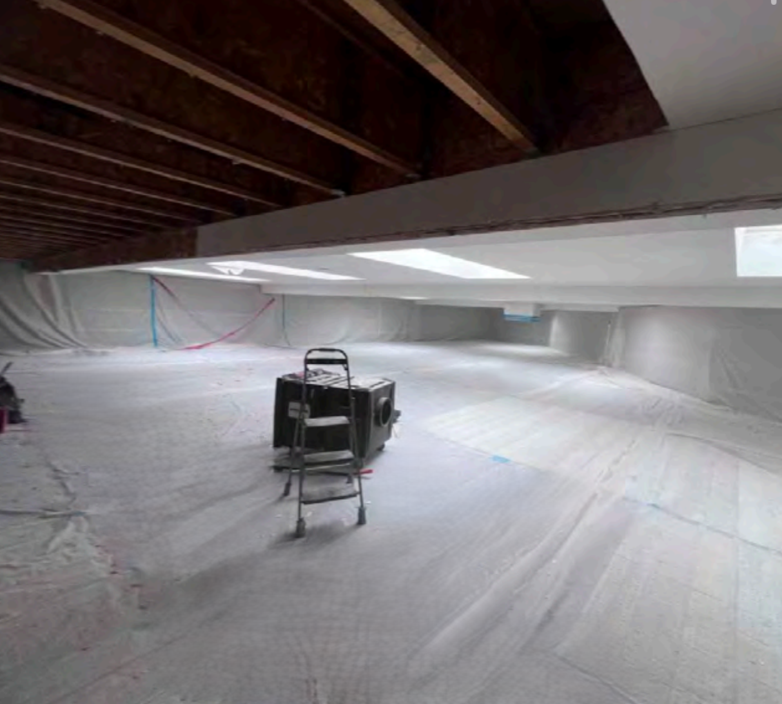 Crawlspace under a house, lined in white plastic, with exposed wooden beams and a tool cart in the center
