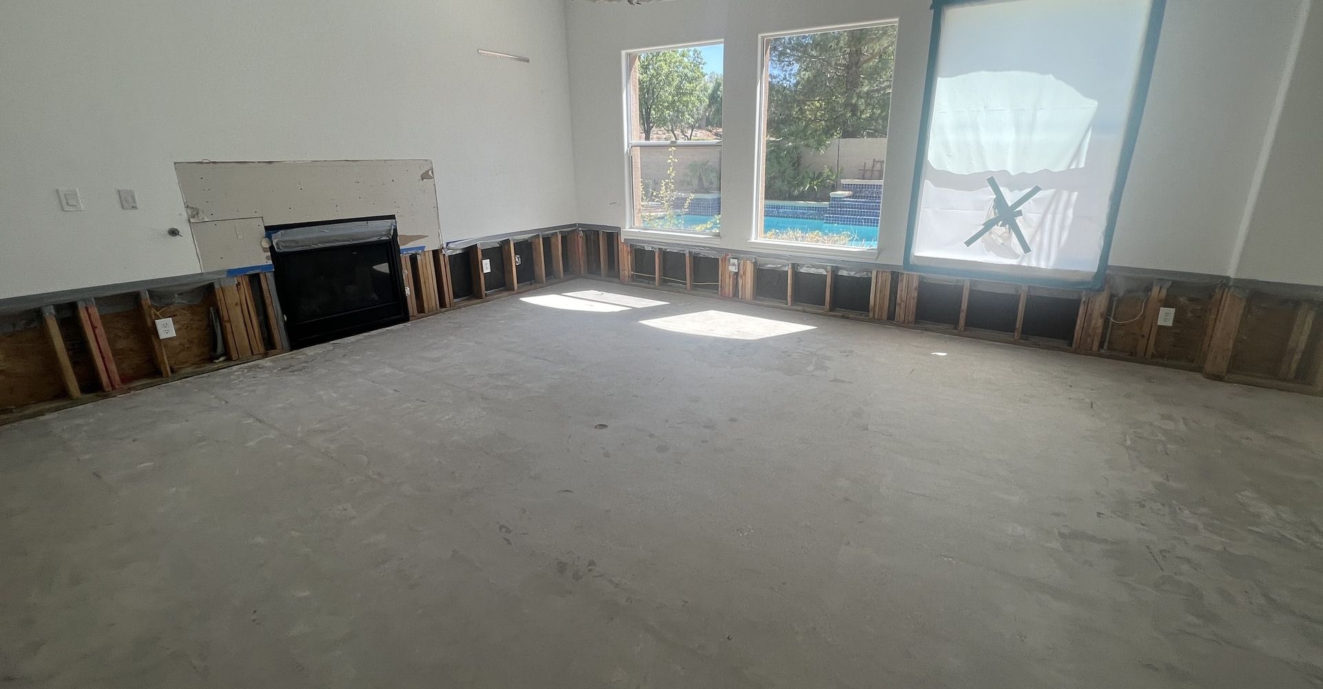 Empty living room with light carpet, dark wood trim, fireplace, and large windows looking out to a pool.