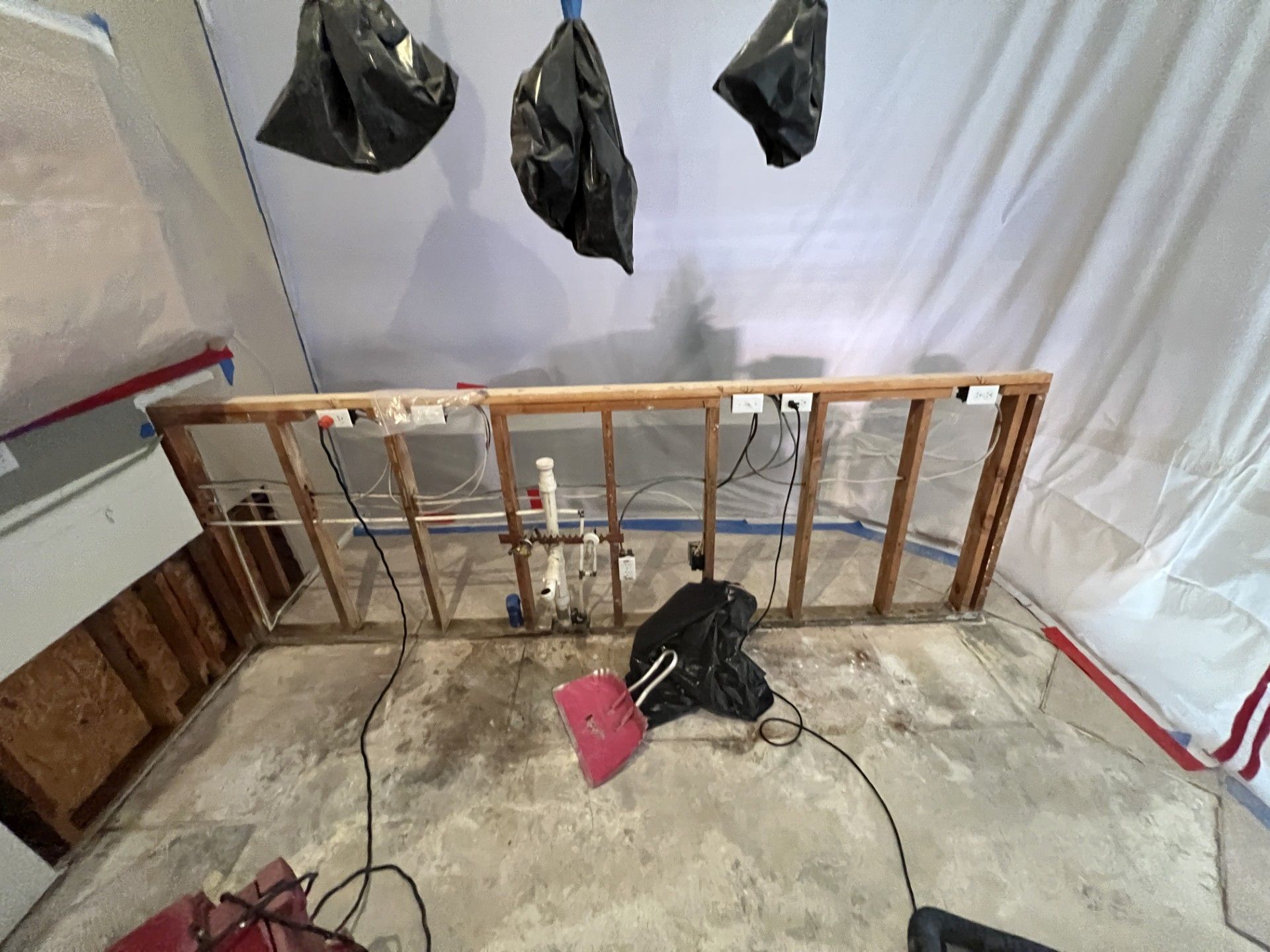 Partially demolished room with exposed wall framing, debris on the floor, and a pink shovel