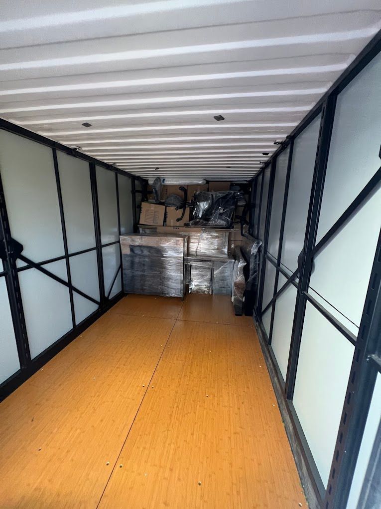 Inside an empty moving truck with wood floor and stacked wrapped furniture at the far end.