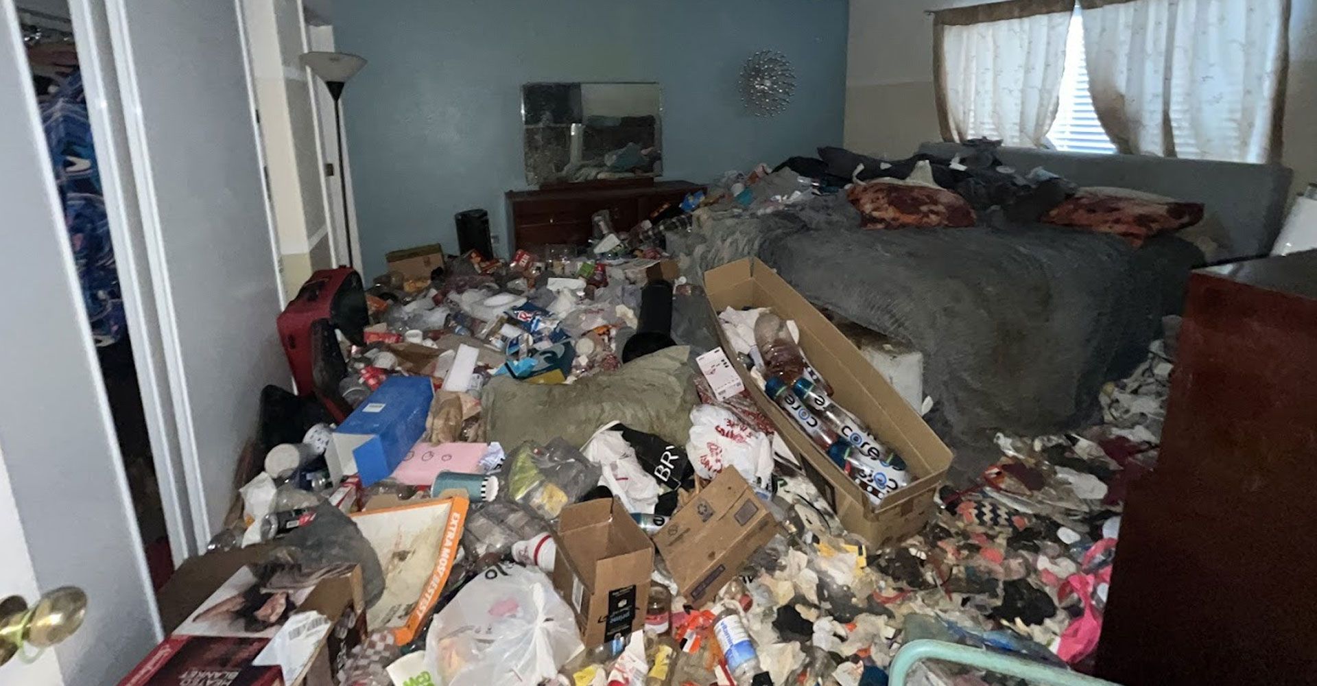 Cluttered living room filled with piles of trash and household debris, with a couch in the back.