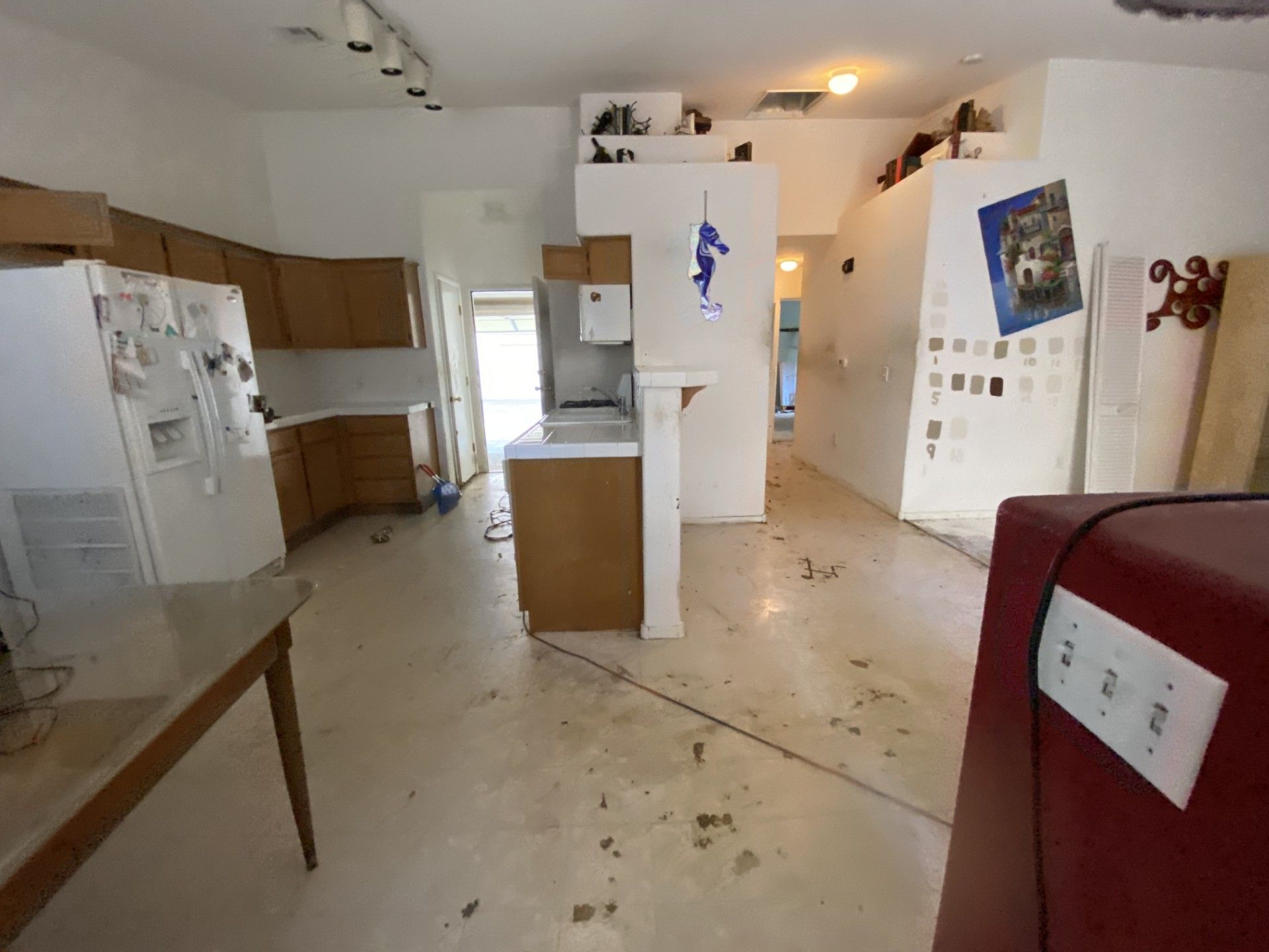 Empty kitchen with white cabinets, a refrigerator, and scattered debris on the floor