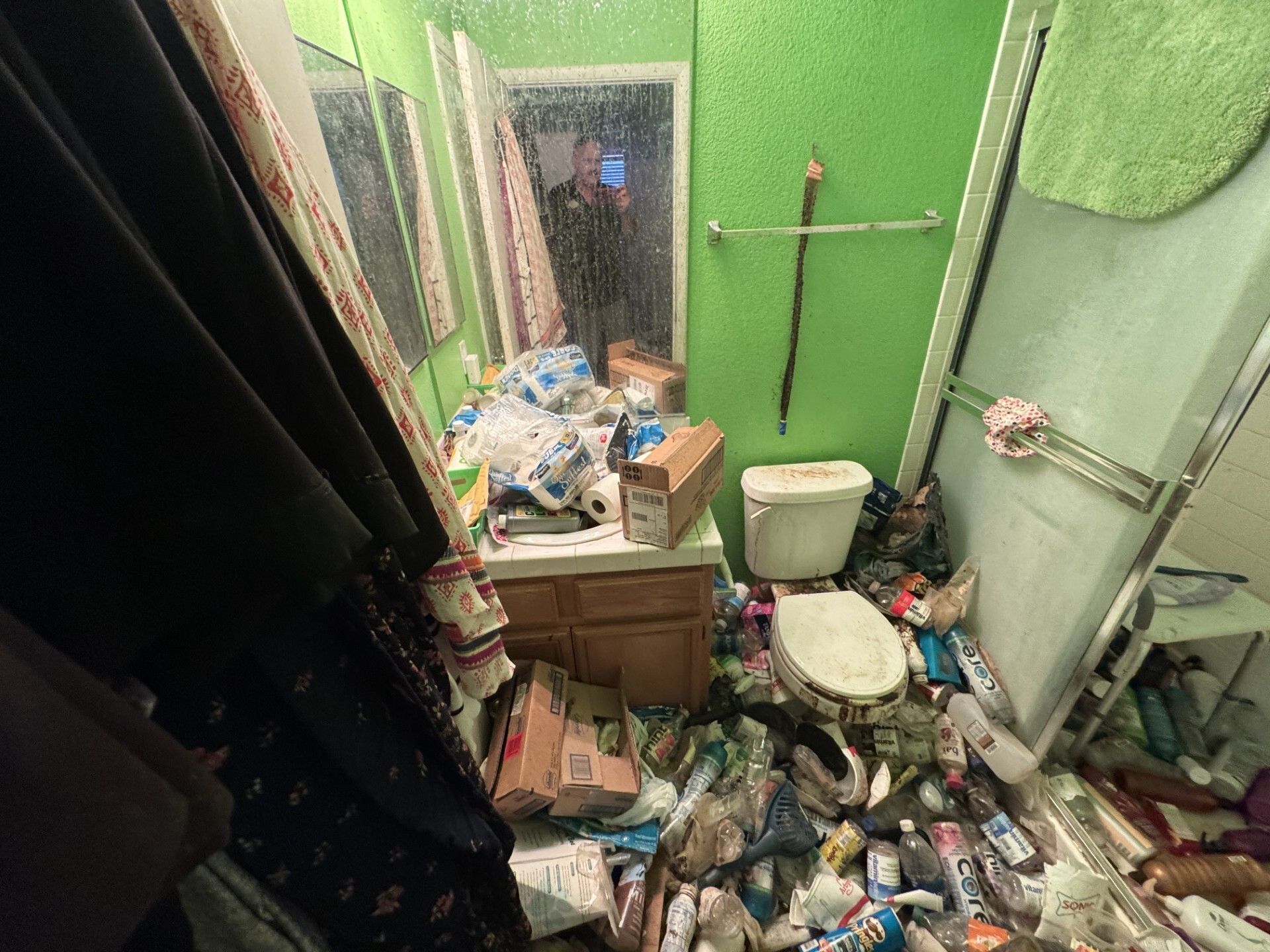 Cluttered green bathroom with trash, debris, a toilet, and a broken sink mirror.