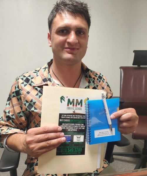 Man holding file, notebook, and pen. Wearing patterned shirt, smiling in office setting.