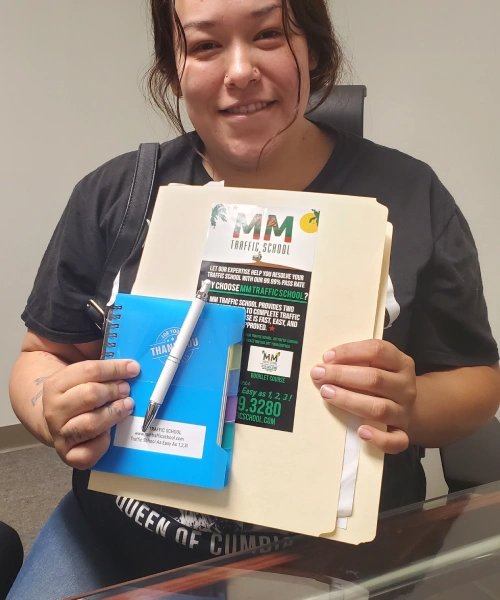 Woman smiling, holding a notepad, pen, and files with stickers. Indoors, wearing black shirt.
