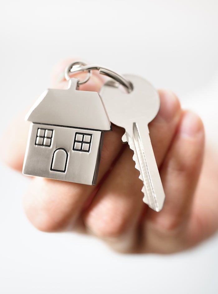 A person is holding a key with a house keychain attached to it.