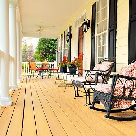 A porch with rocking chairs , a table and chairs on it.