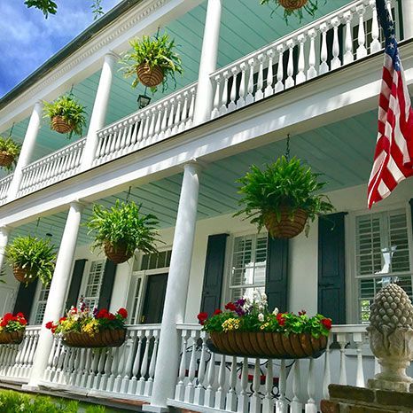 A large white house with a porch covered in potted plants and flowers