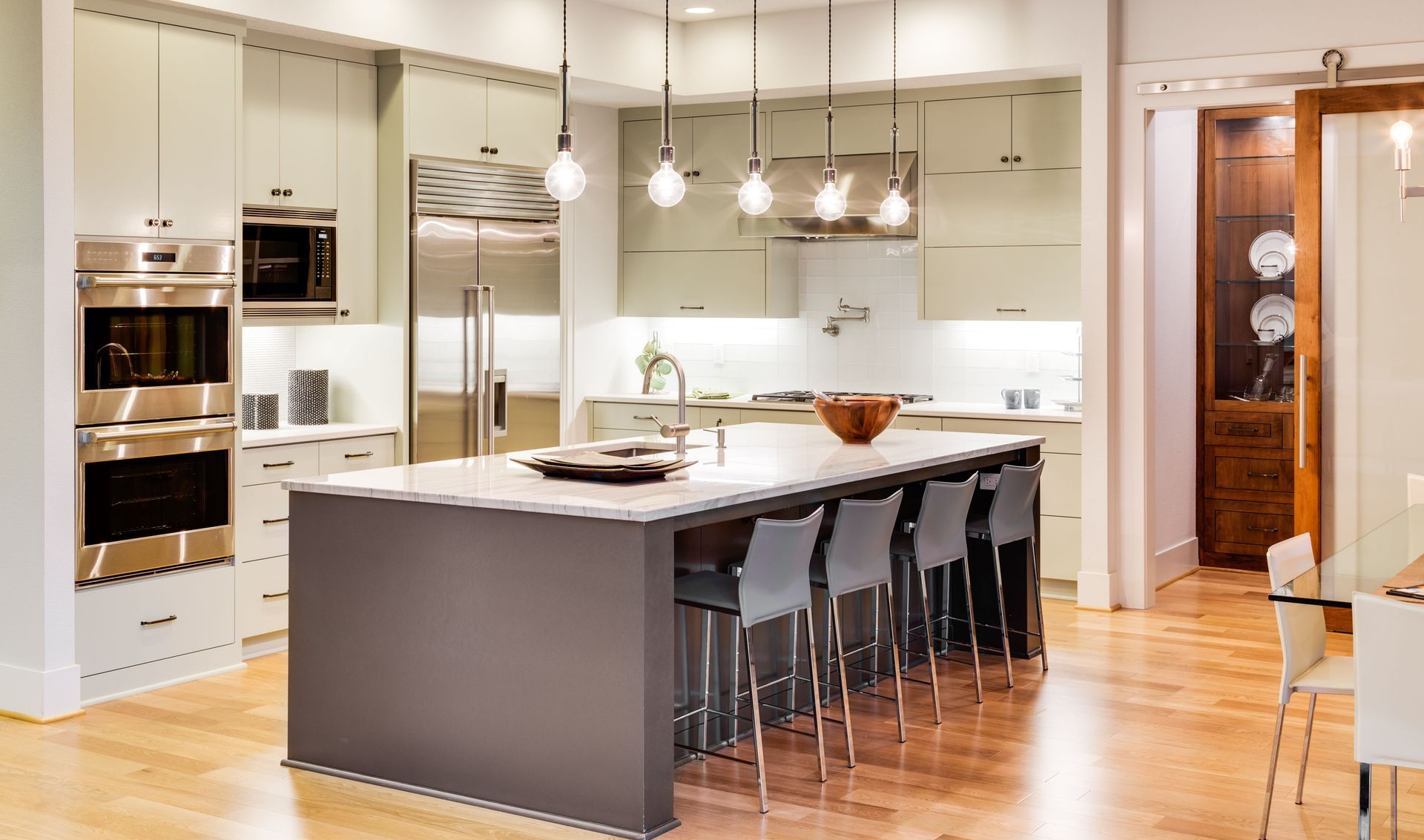 Modern kitchen with island, stainless steel appliances, pendant lights, and bar stools.