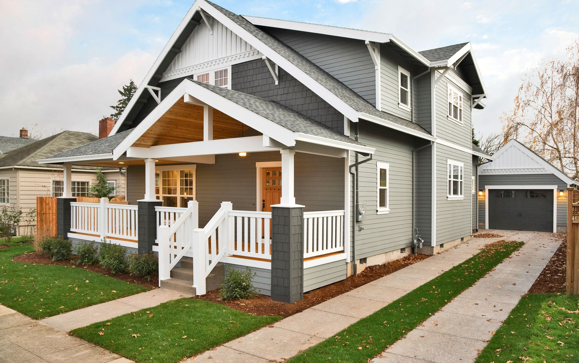 Gray craftsman-style house with white trim, porch, and attached garage. Green lawn and driveway.