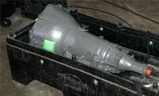 Transparent black plastic bottle in a black crate, lying on its side with a green label and orange cap