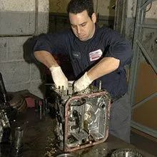 Mechanic in dark coveralls repairing a metal machine in a workshop, hands inside the open casing