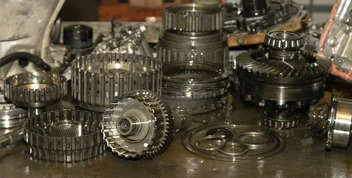 Pile of metallic gears and mechanical parts on a workbench, with gears stacked and scattered in a workshop.