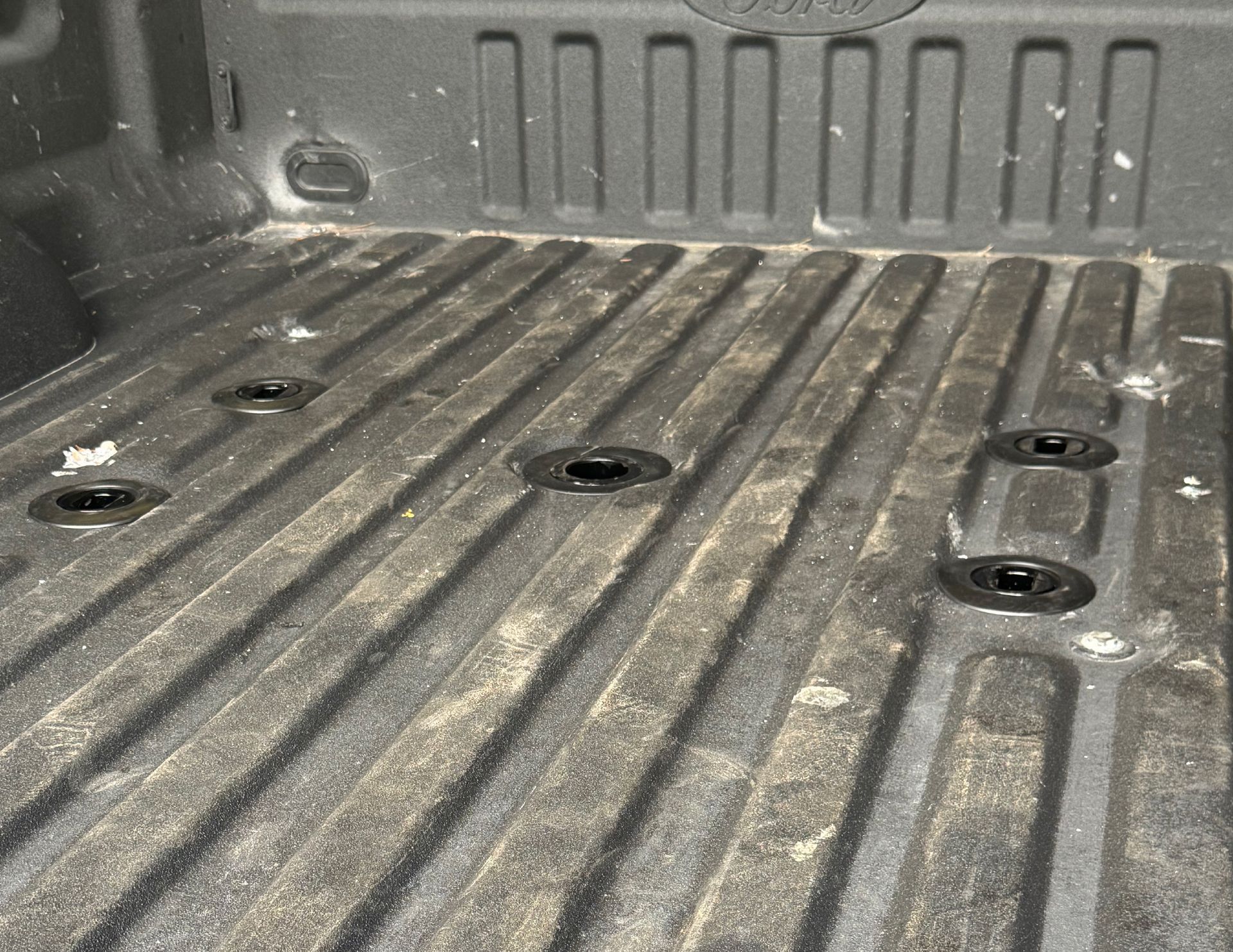 Truck bed with Ford logo and recessed tie-down points, covered in light debris.