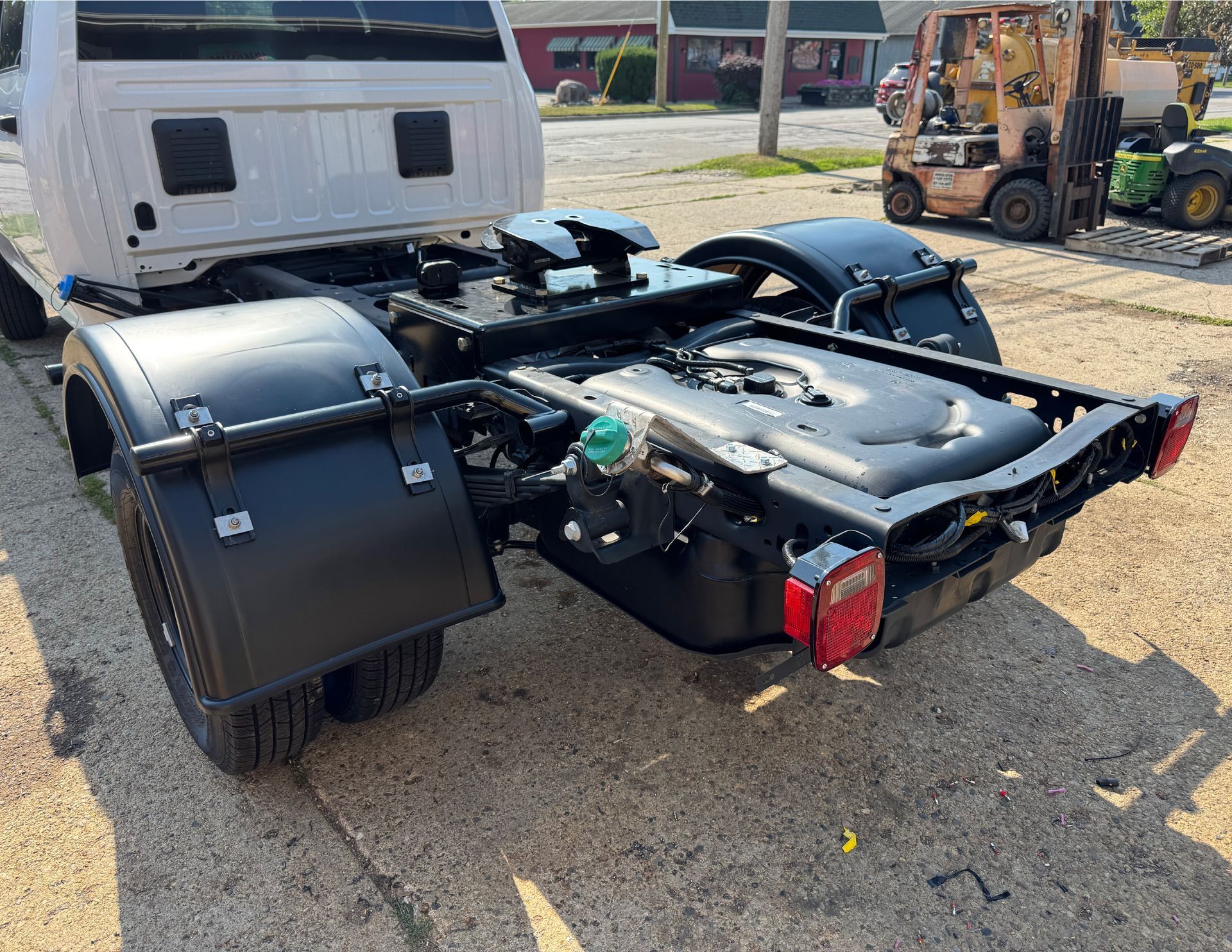 Black chassis of a truck with fenders, a fifth-wheel, and taillights on a paved surface.