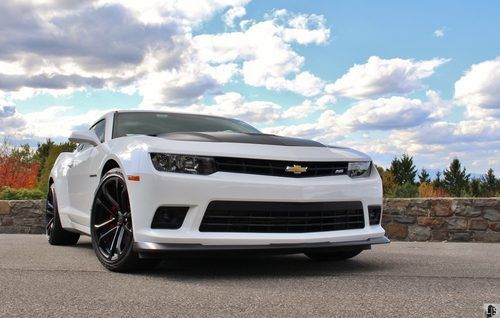 A white chevrolet camaro is parked in front of a stone wall.