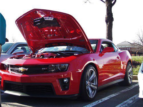 A red car with the hood open is parked in a parking lot.