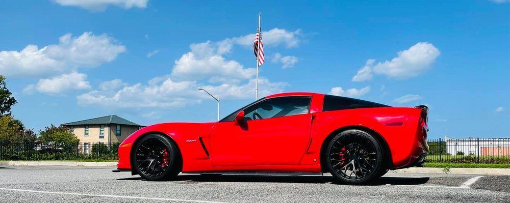 A red sports car is parked on the side of the road in a parking lot.