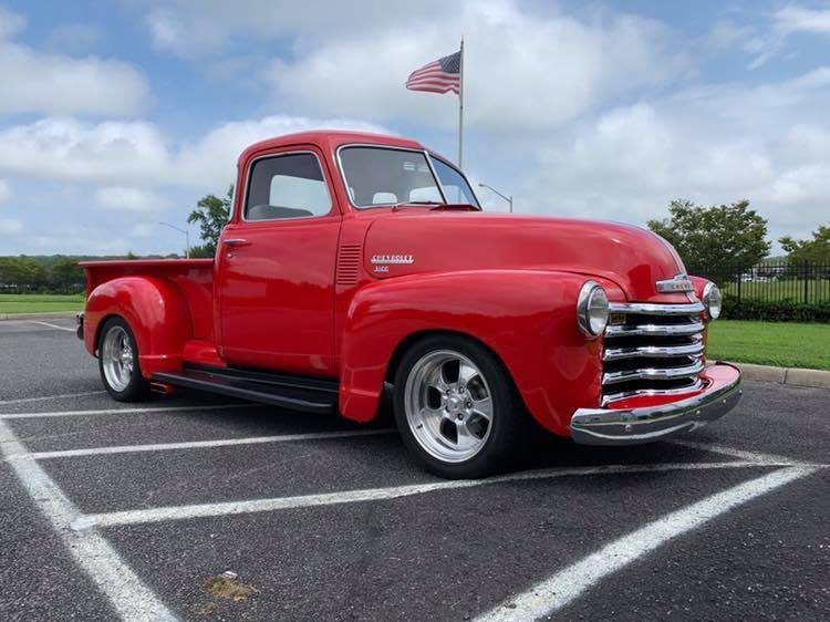A red truck is parked in a parking lot with an american flag in the background.