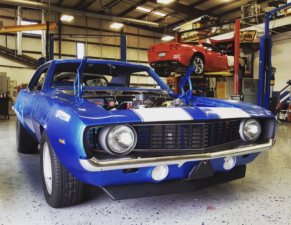 A blue car is parked in a garage with the hood open