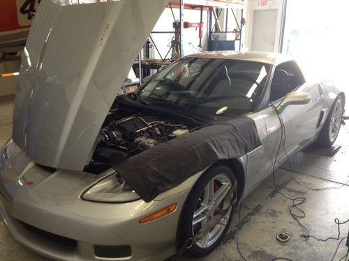A silver sports car with the hood up in a garage