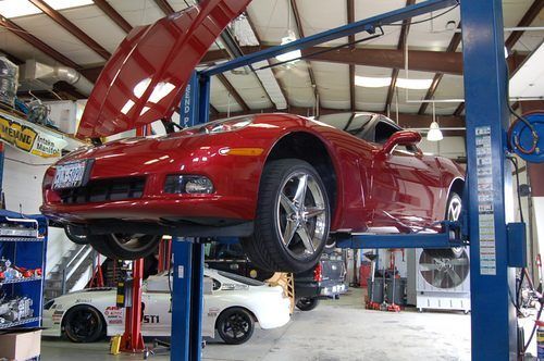A red sports car is on a lift in a garage.