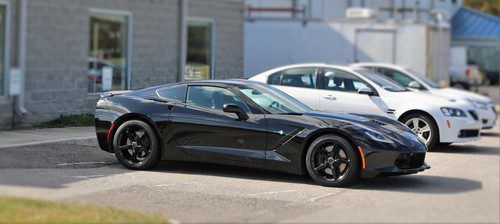 A black corvette is parked next to a white car in a parking lot.