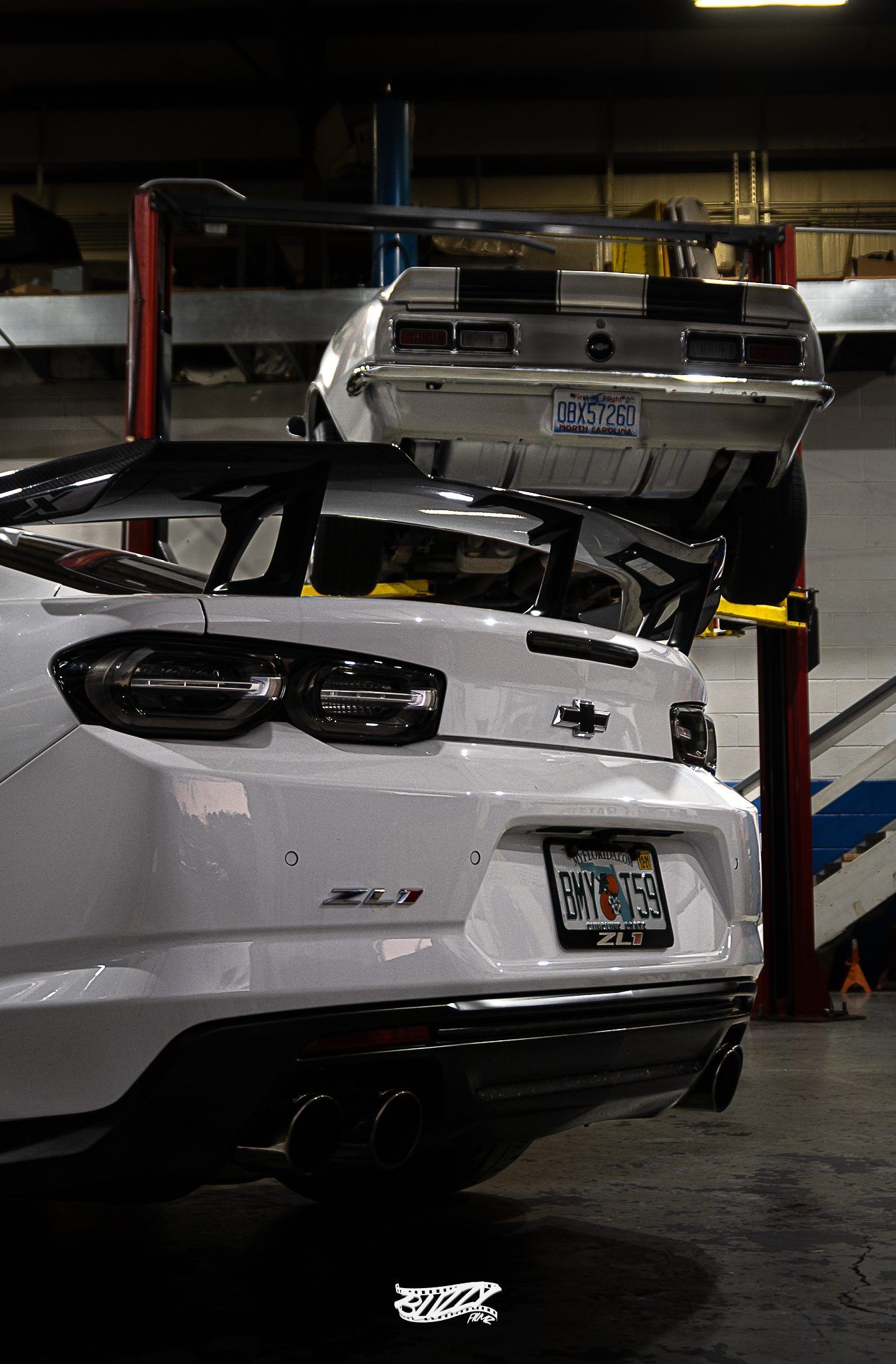 A white car is parked in a garage next to another car