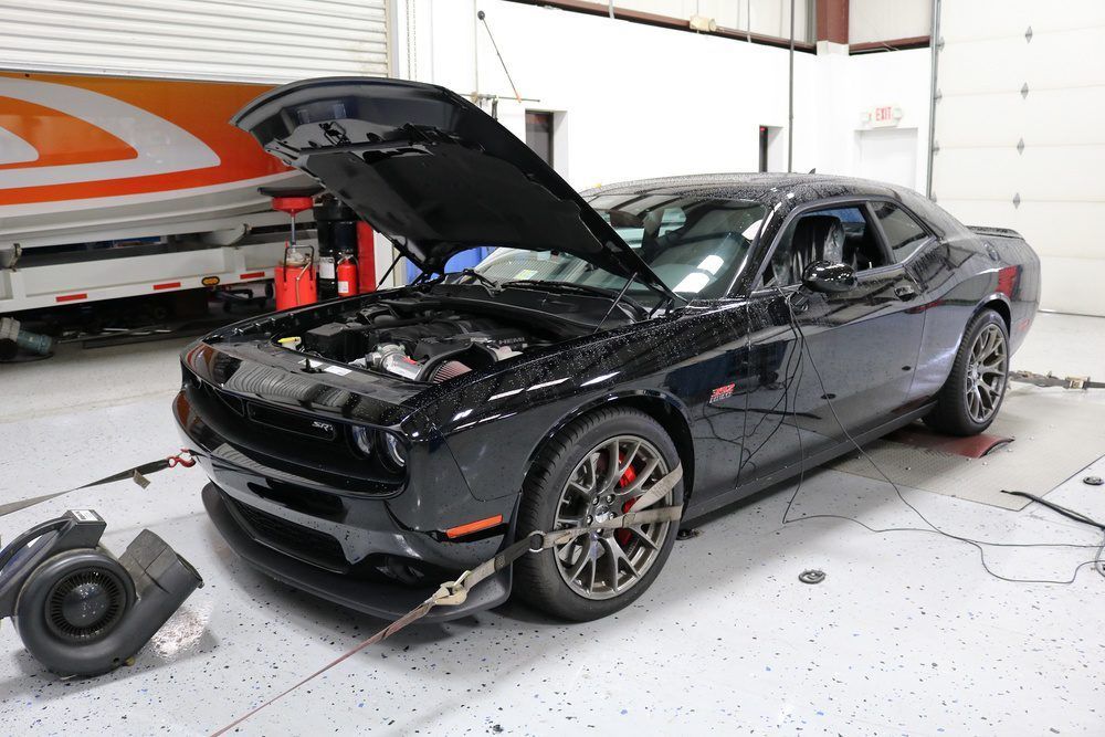 A black dodge challenger with the hood up in a garage