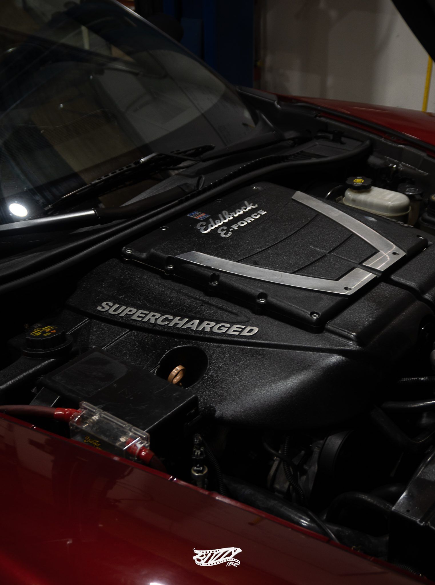The engine of a red sports car is shown with the hood open.