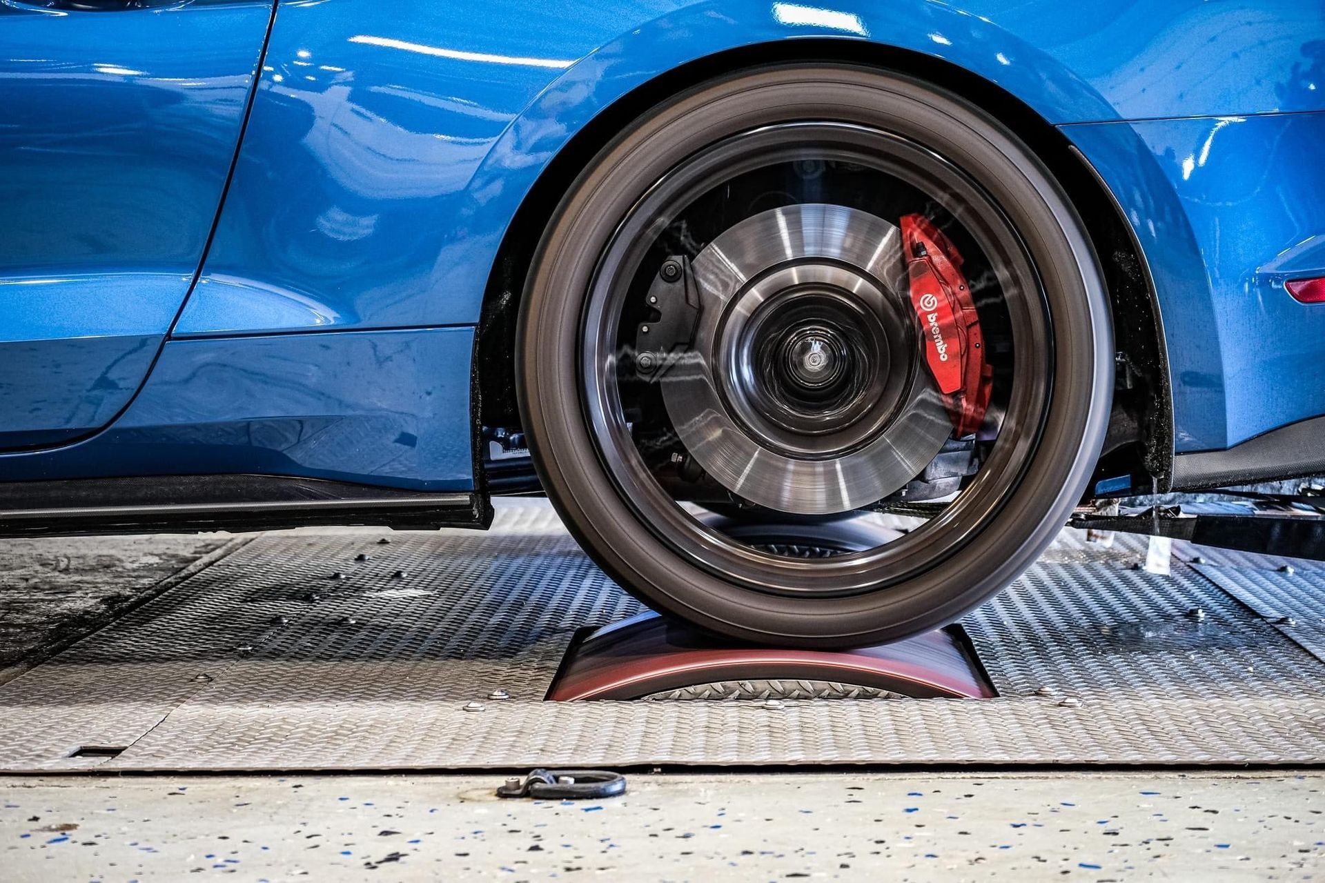 A blue mustang is being tested on a dyno in a garage.