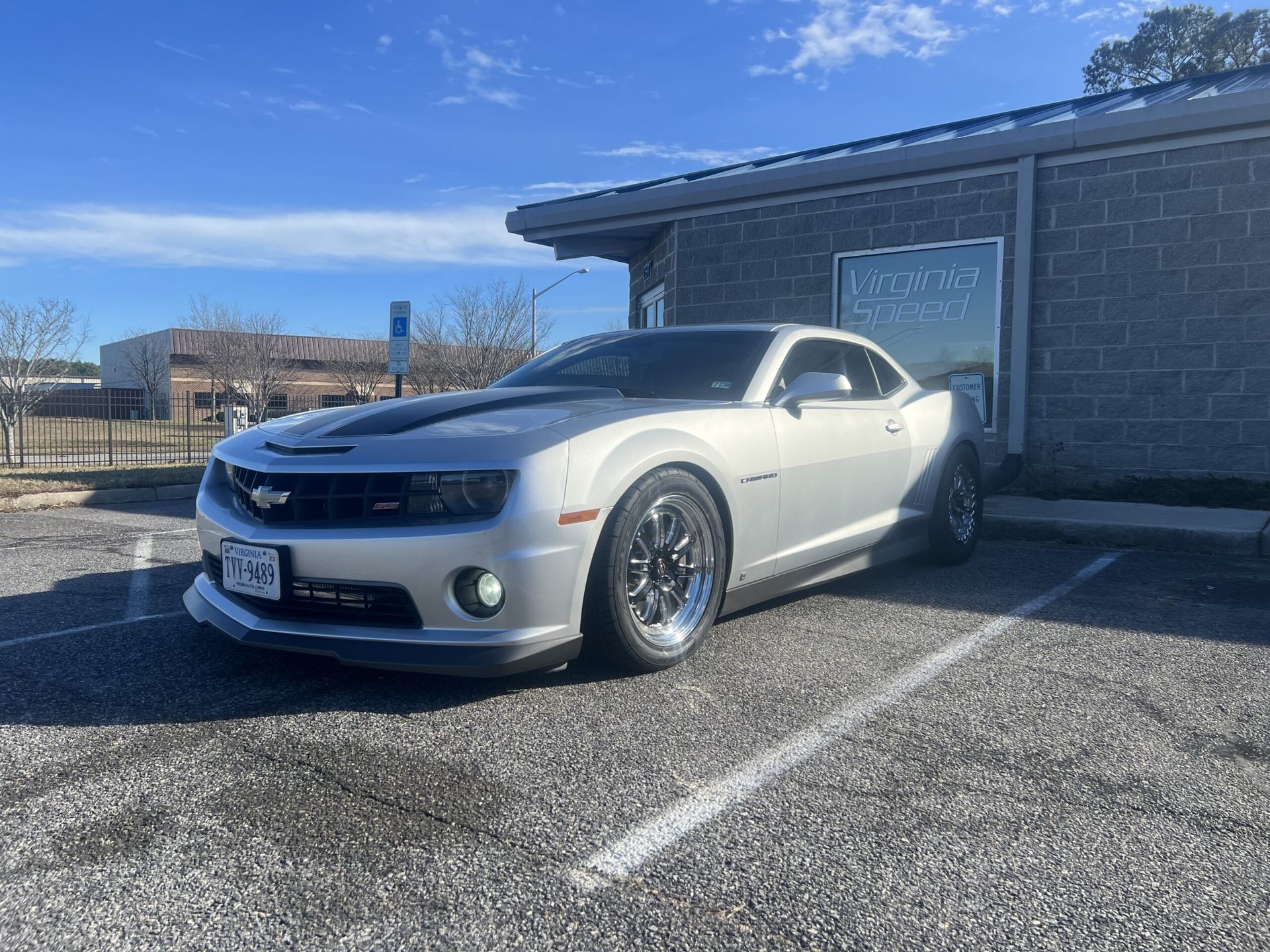 A silver car is parked in a parking lot in front of a building.