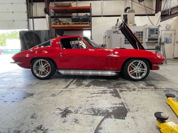A red car with the hood up is parked in a garage