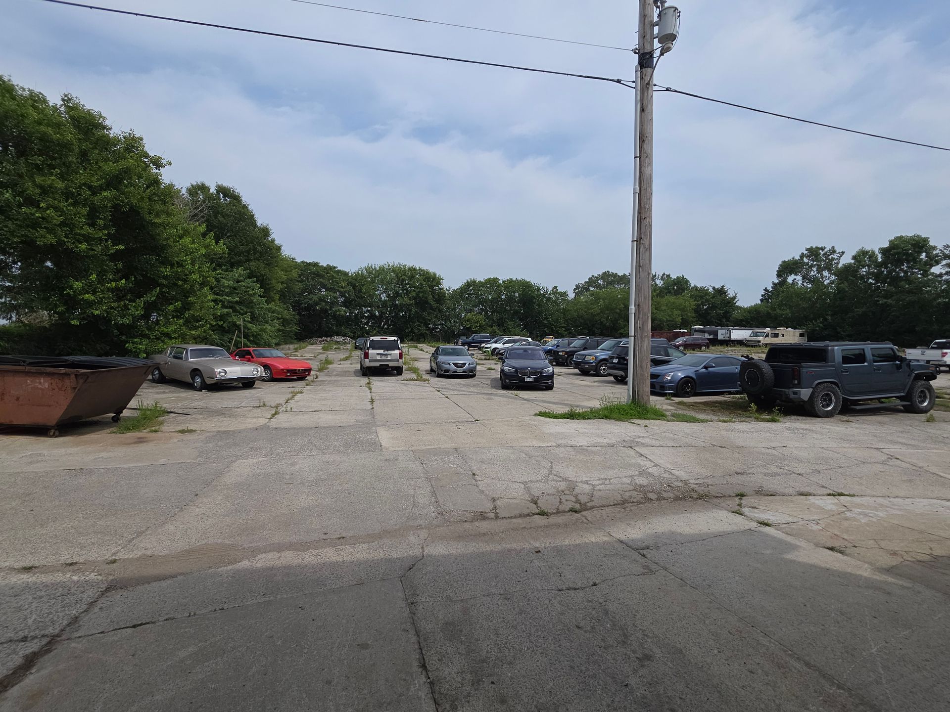 Parking lot with several cars and trucks beside trees and a utility pole under a cloudy sky