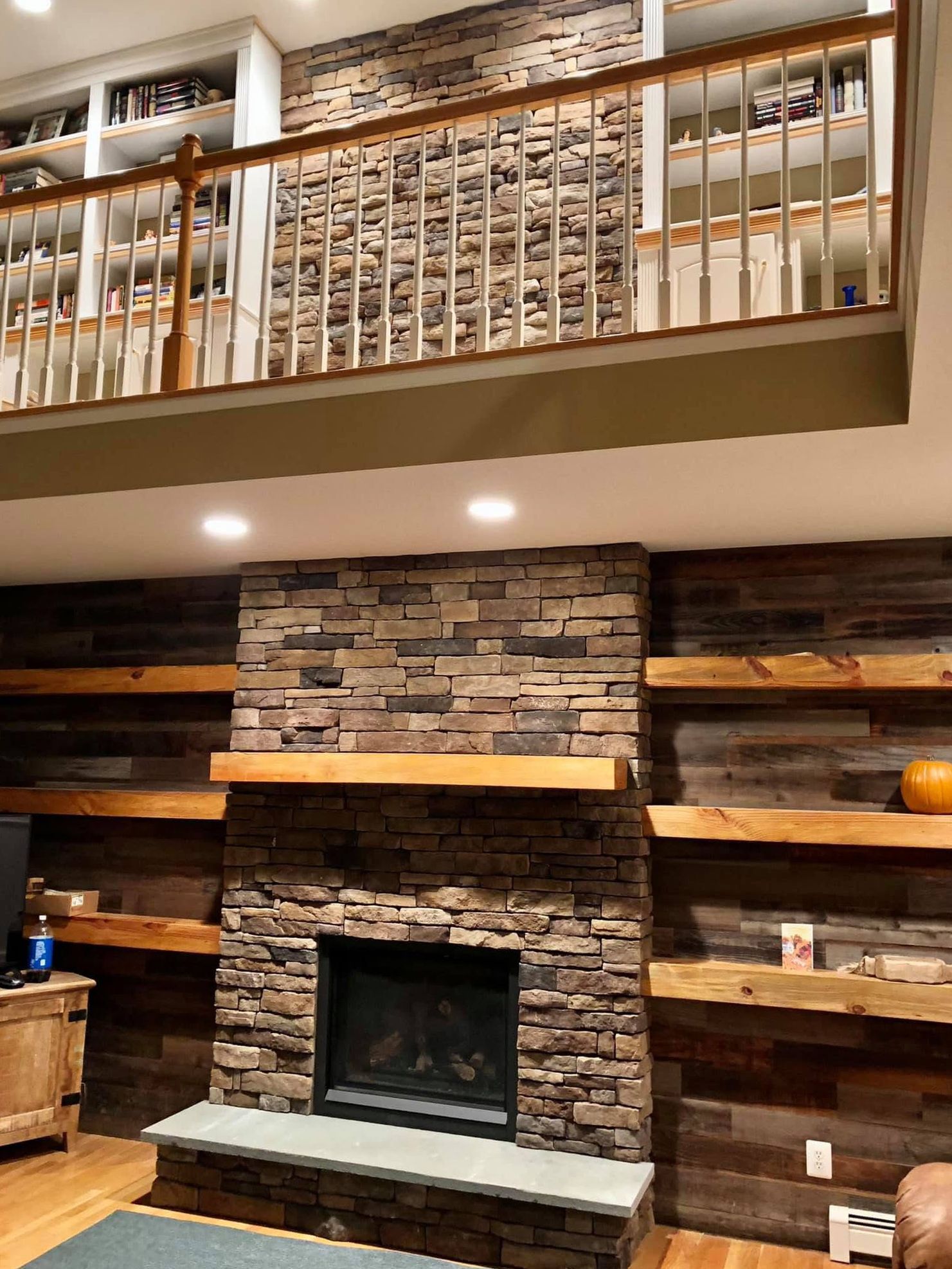 A living room with a stone fireplace and wooden shelves.