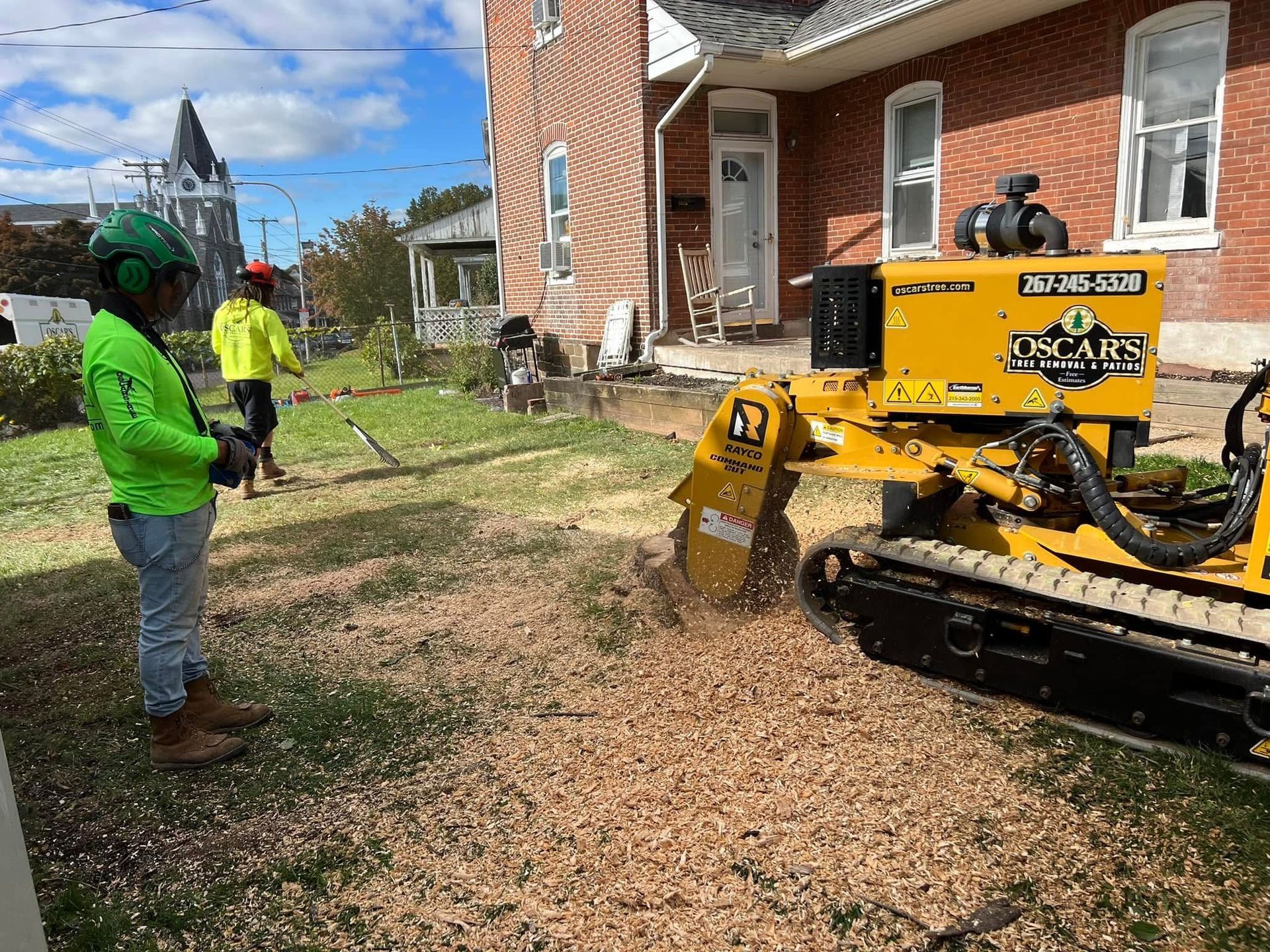 A stump grinder is being used to remove a tree stump in front of a brick building.