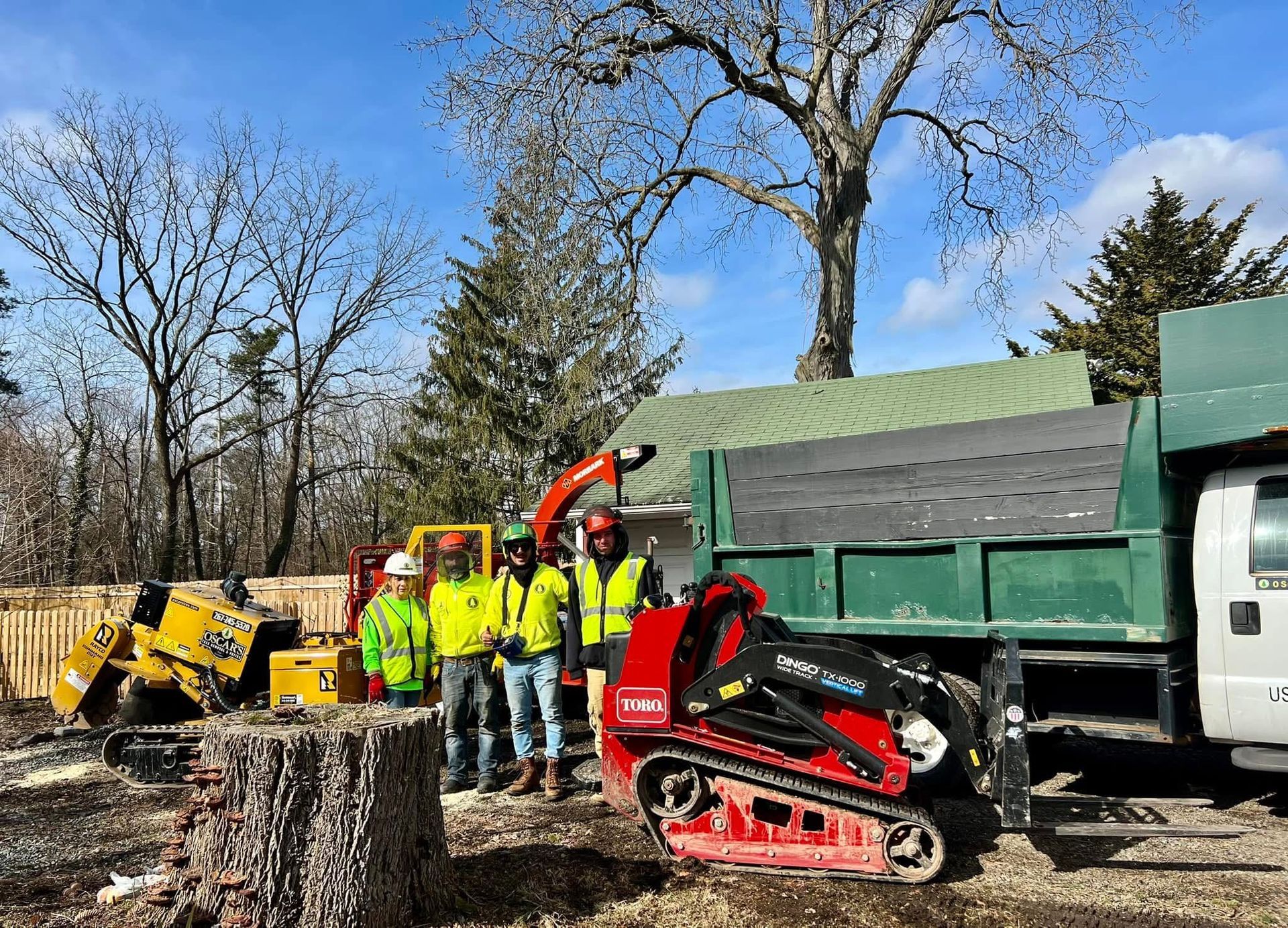 A group of men are standing next to a tree stump and a dump truck.