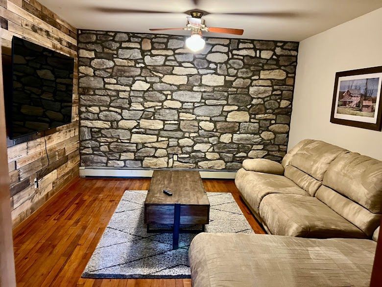 A living room with a stone wall , a couch , a coffee table and a flat screen tv.