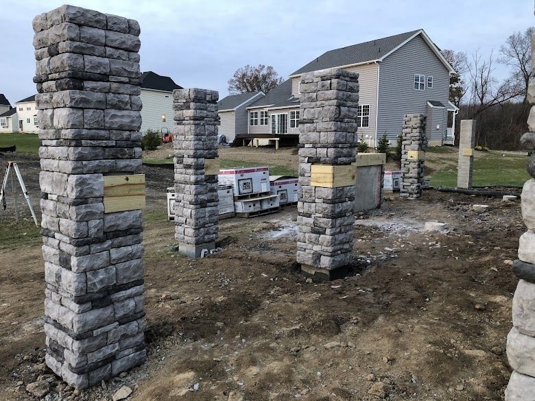 A row of stone pillars are sitting in the dirt in front of a house.