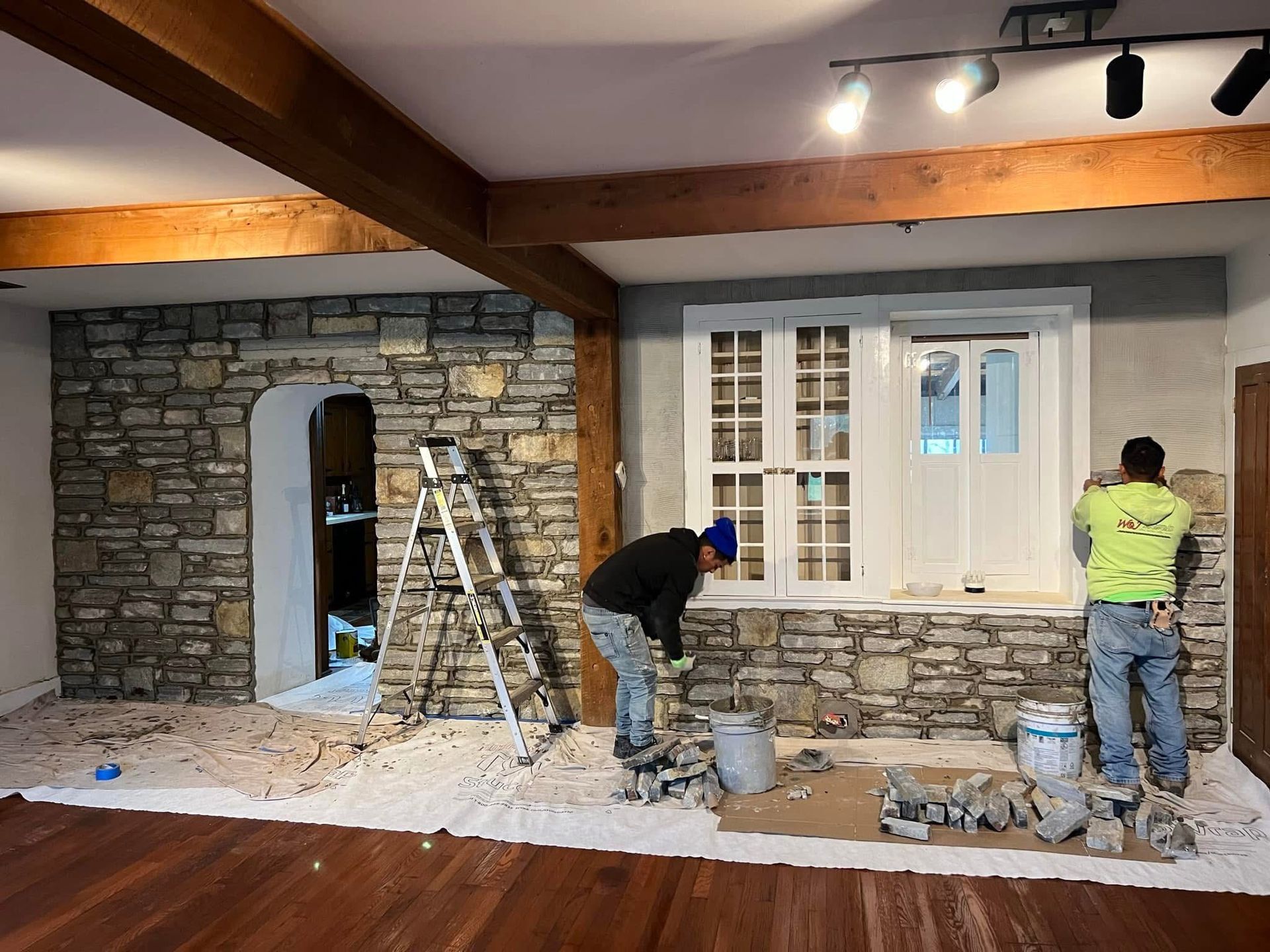Two men are working on a stone wall in a living room.