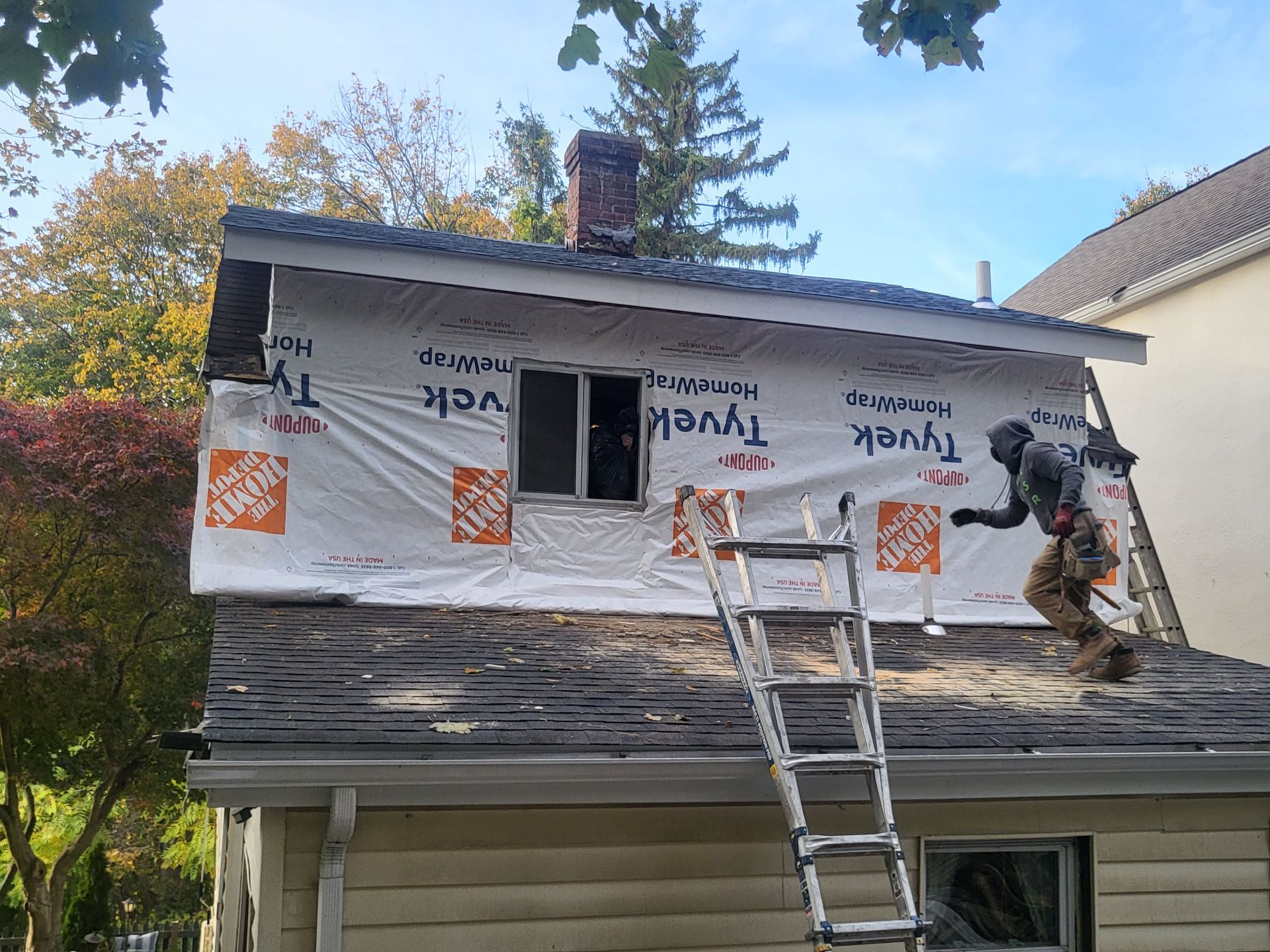 a man is standing on a ladder on the roof of a residential house