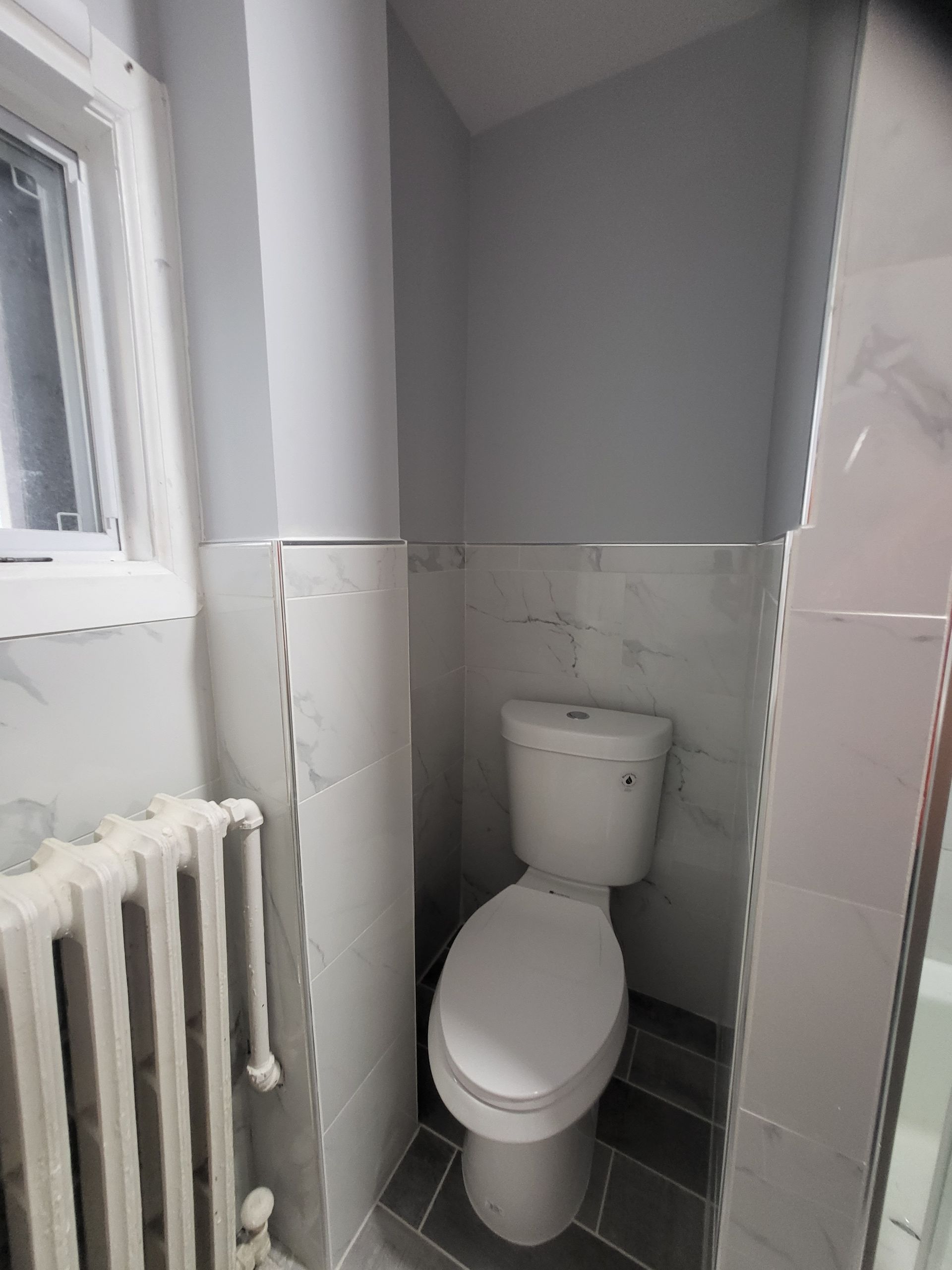 a bathroom with a toilet, radiator, and window