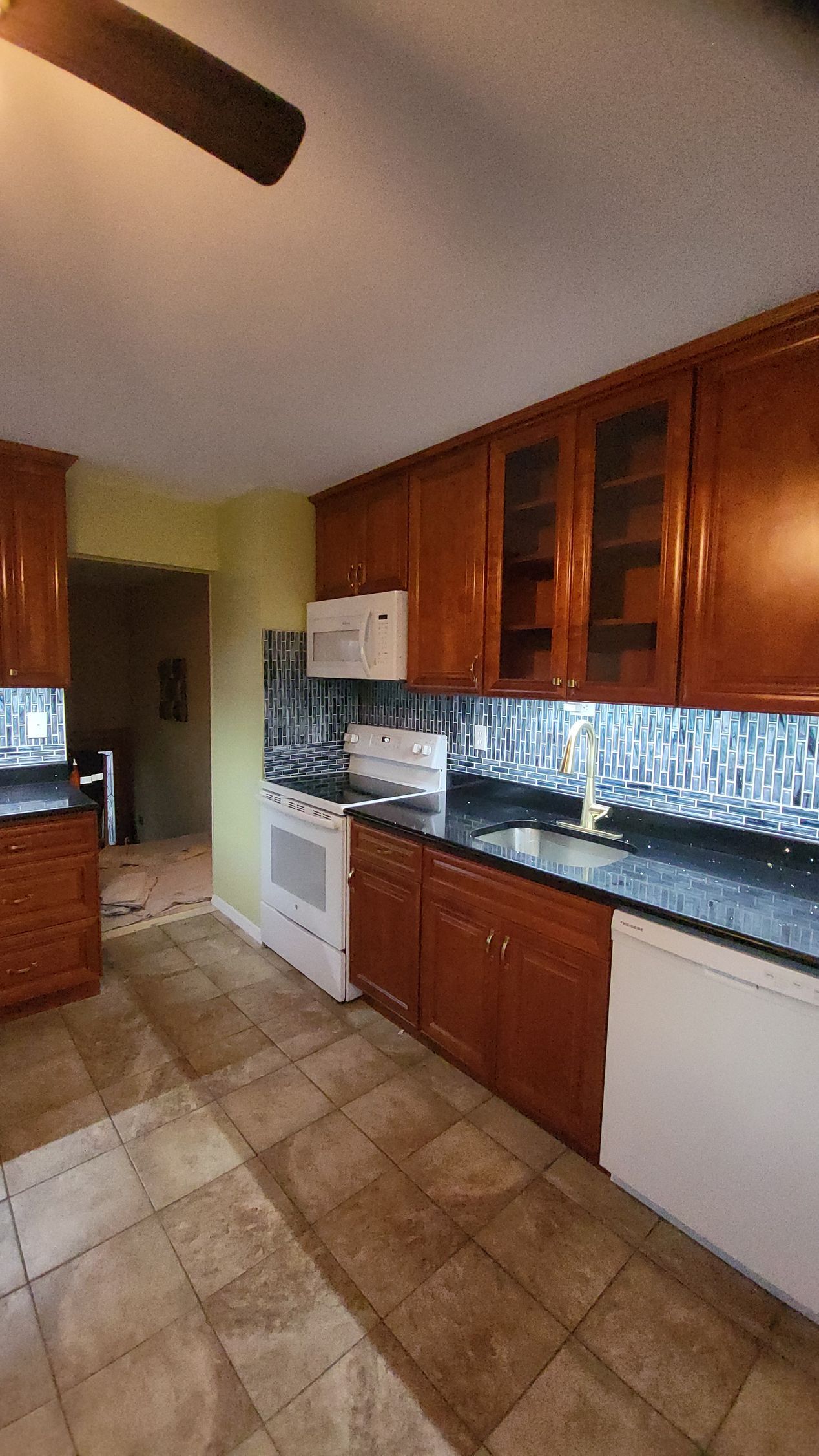 a kitchen with wooden cabinets, granite counter tops, a stove, and a ceiling fan